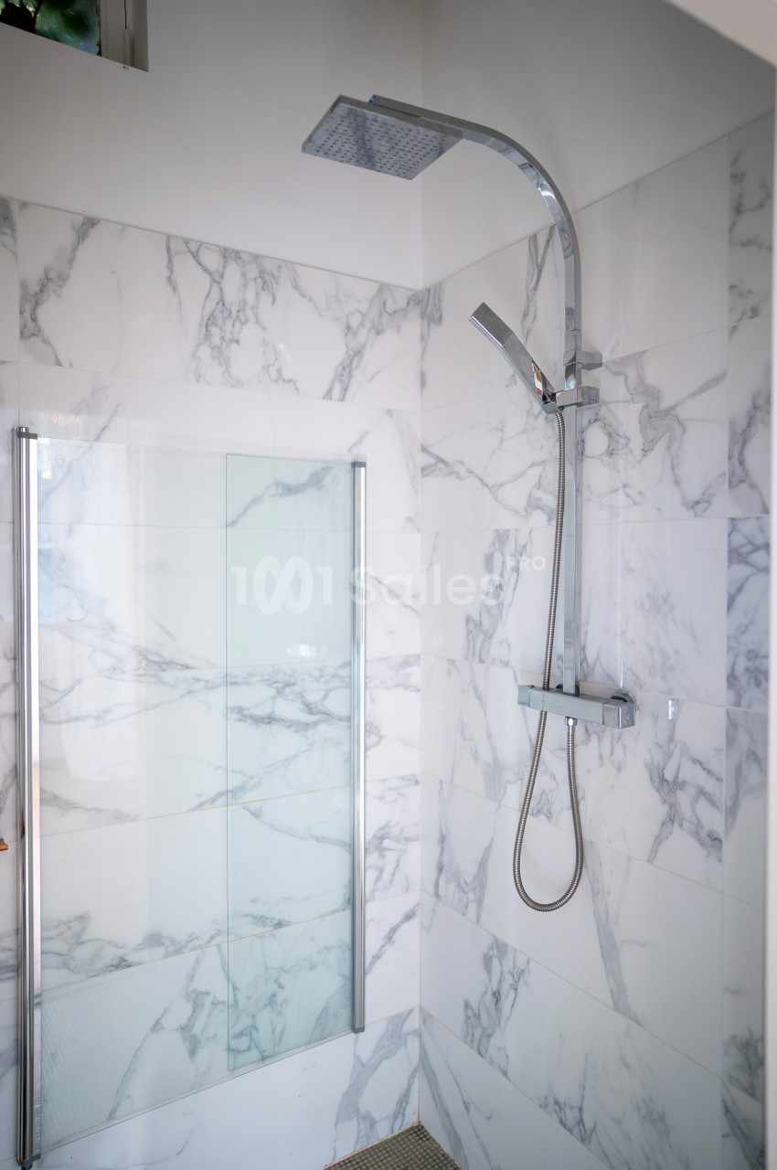 Douche moderne avec paroi en verre et carrelage effet marbre, équipée d'une colonne de douche chromée.