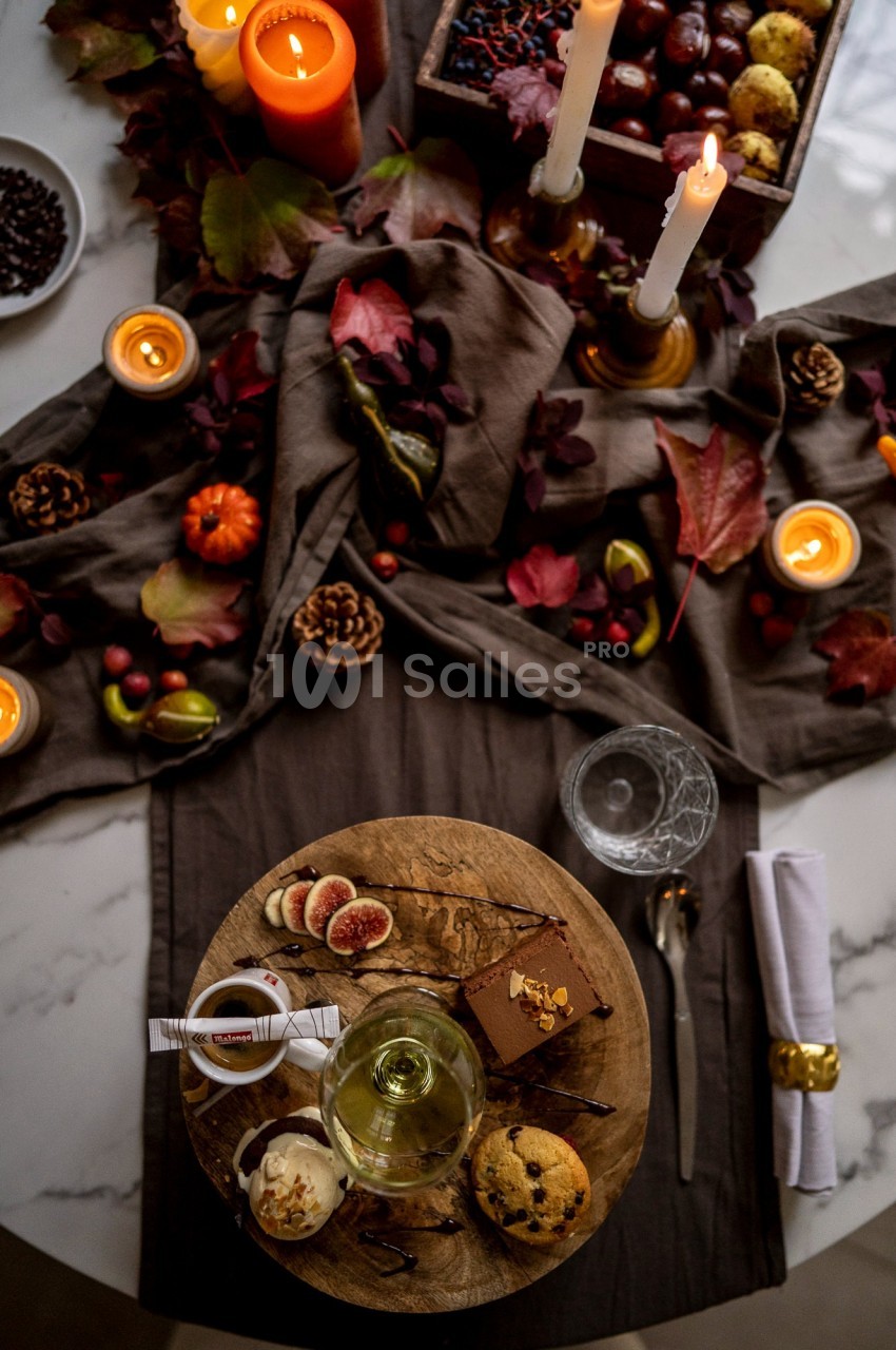 Table décorée avec des bougies, feuilles d'automne, fruits, et dessert servi avec verre de vin et couverts.
