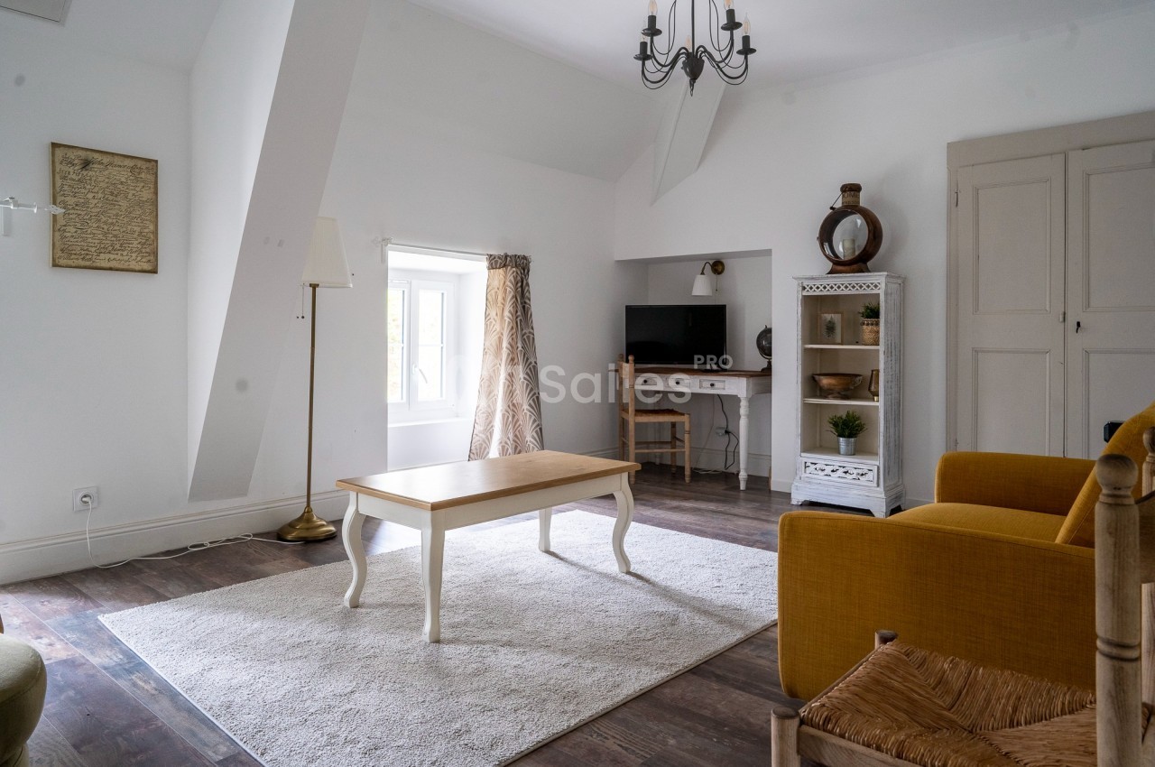 Salon lumineux avec parquet, tapis clair, table basse, fauteuils jaunes, bureau avec écran et étagères décoratives.