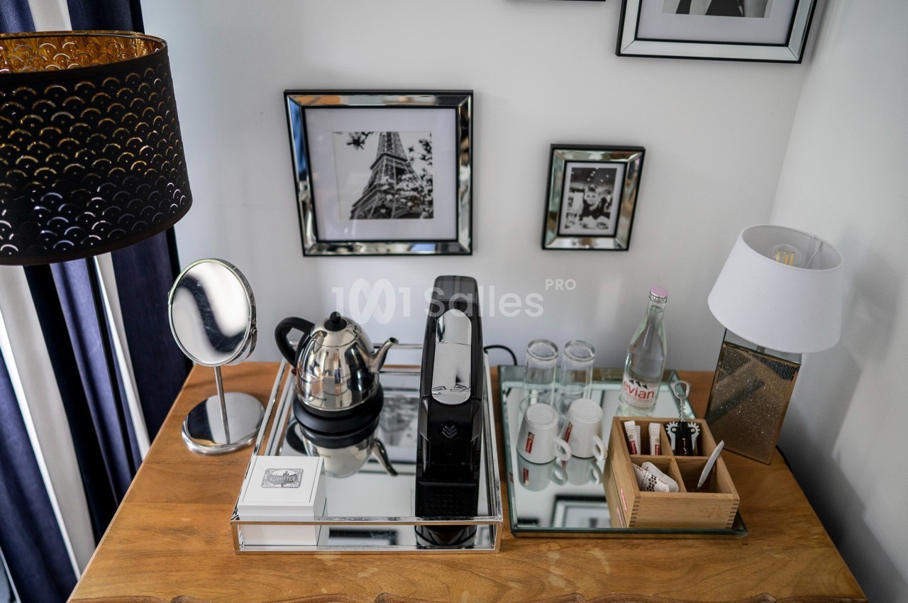 Plateau de courtoisie avec machine à café, bouilloire, verres, bouteilles d'eau et accessoires sur une table en bois.