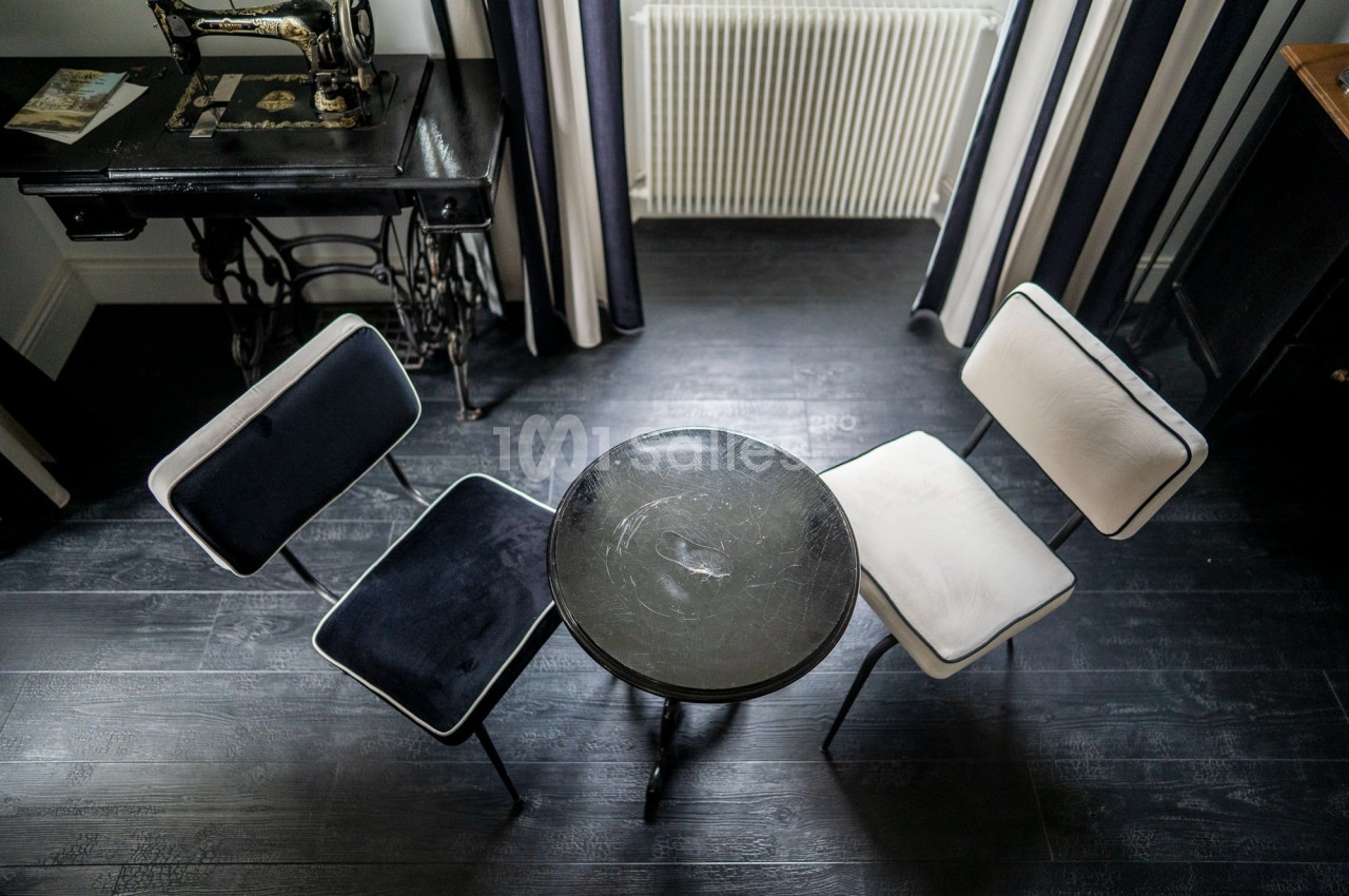 Deux chaises, une noire et une blanche, entourent une petite table ronde sur un sol en bois sombre.