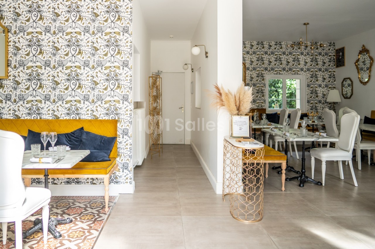 Salle lumineuse avec décoration élégante, murs ornés de papier peint à motifs, mobilier blanc et touches dorées.