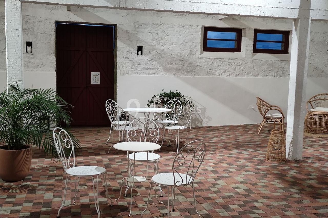 Terrasse intérieure avec tables et chaises en fer forgé, sol en carreaux colorés et murs blancs.