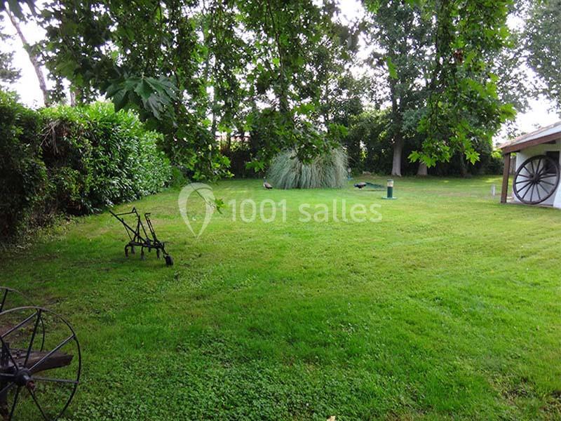 Un jardin verdoyant avec pelouse, arbres, arbustes et une charrette ancienne près d'un abri en bois.
