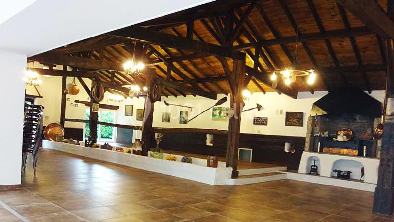 Salle spacieuse avec charpente en bois apparente, décor rustique, cheminée et objets traditionnels accrochés aux murs.