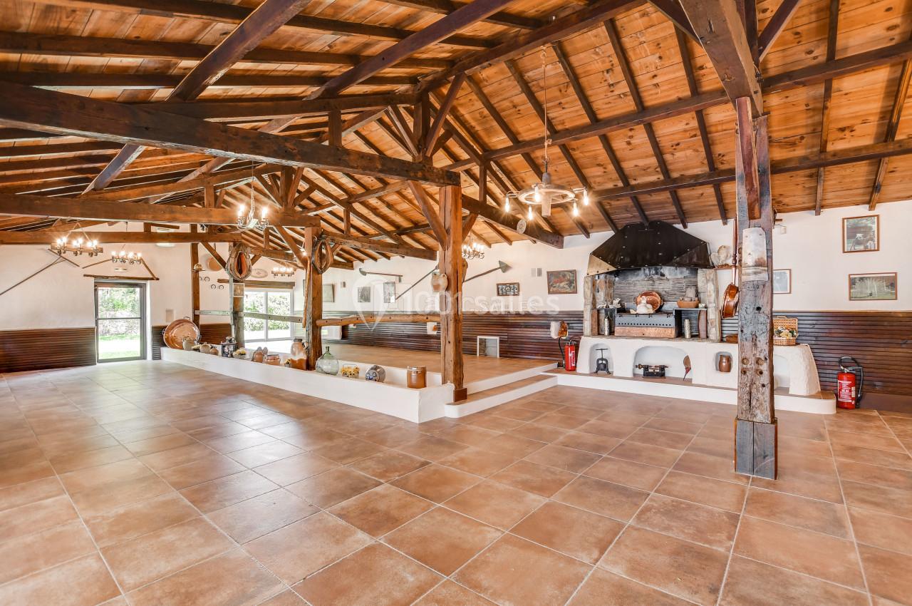 Salle spacieuse avec plafond en bois, carrelage au sol, cheminée en pierre et décorations rustiques sur les murs.