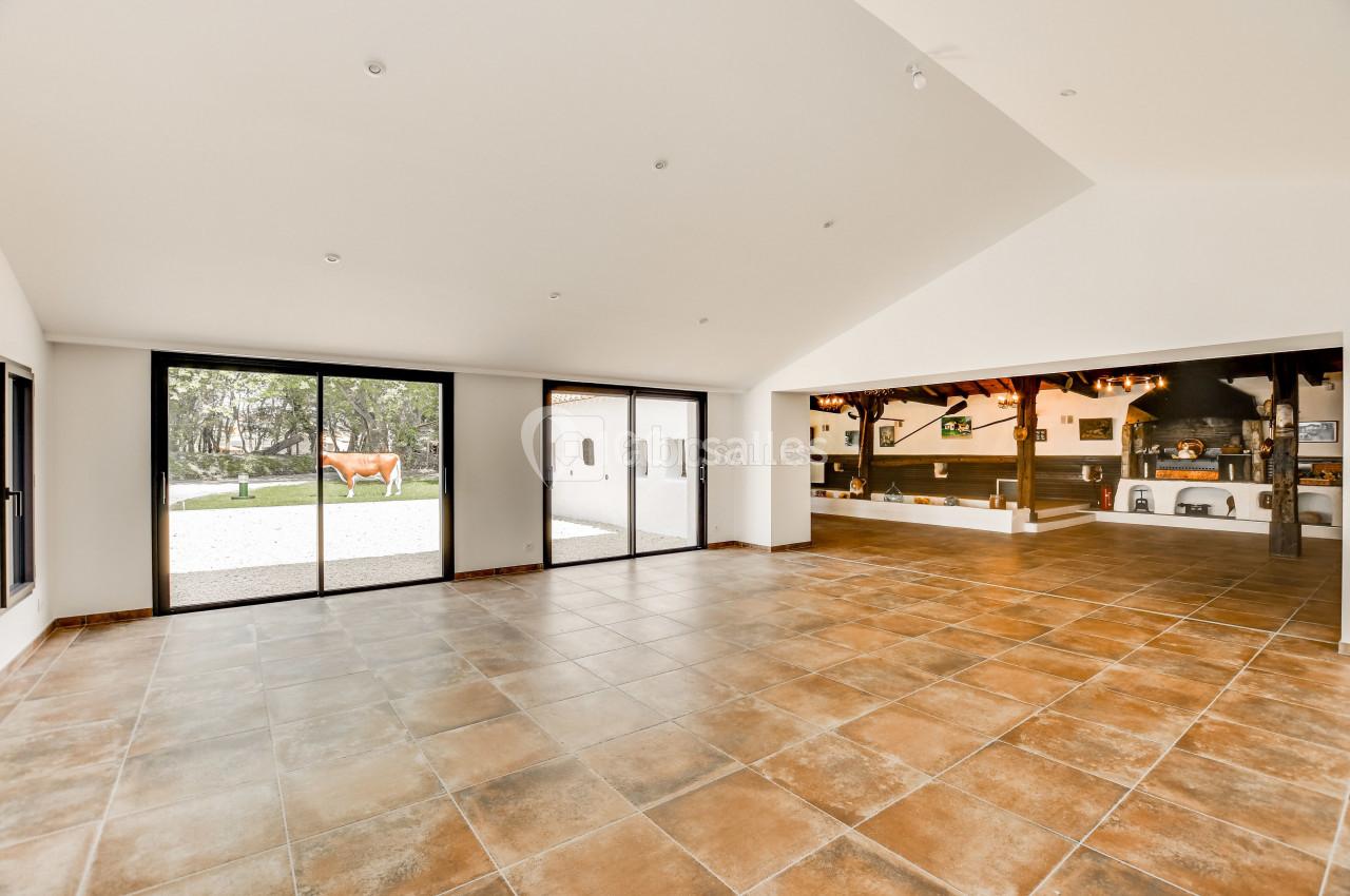 Salle spacieuse avec sol en carrelage, grandes baies vitrées donnant sur un extérieur arboré et espace cuisine ouvert.