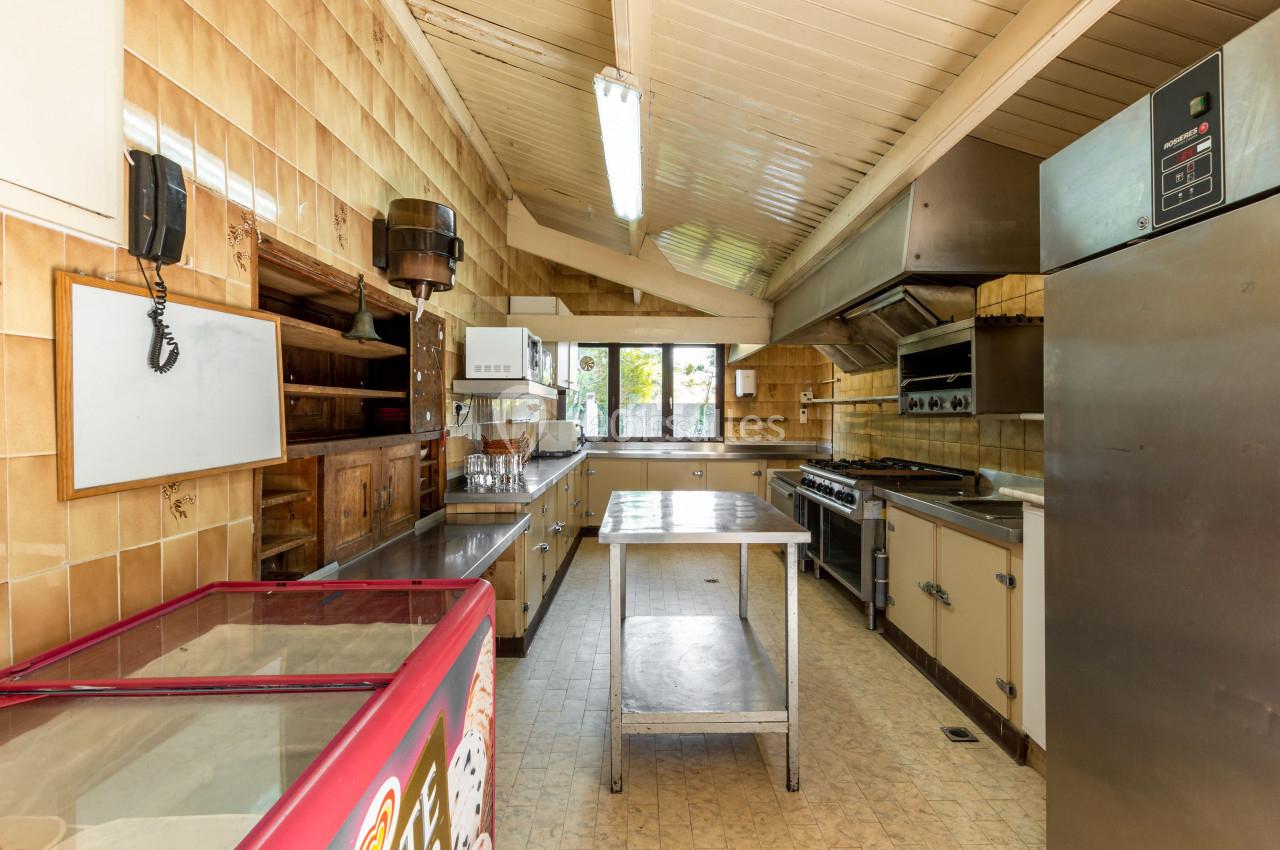 Cuisine professionnelle équipée avec plans de travail en inox, appareils de cuisson et rangements, éclairée par une fenêtre.