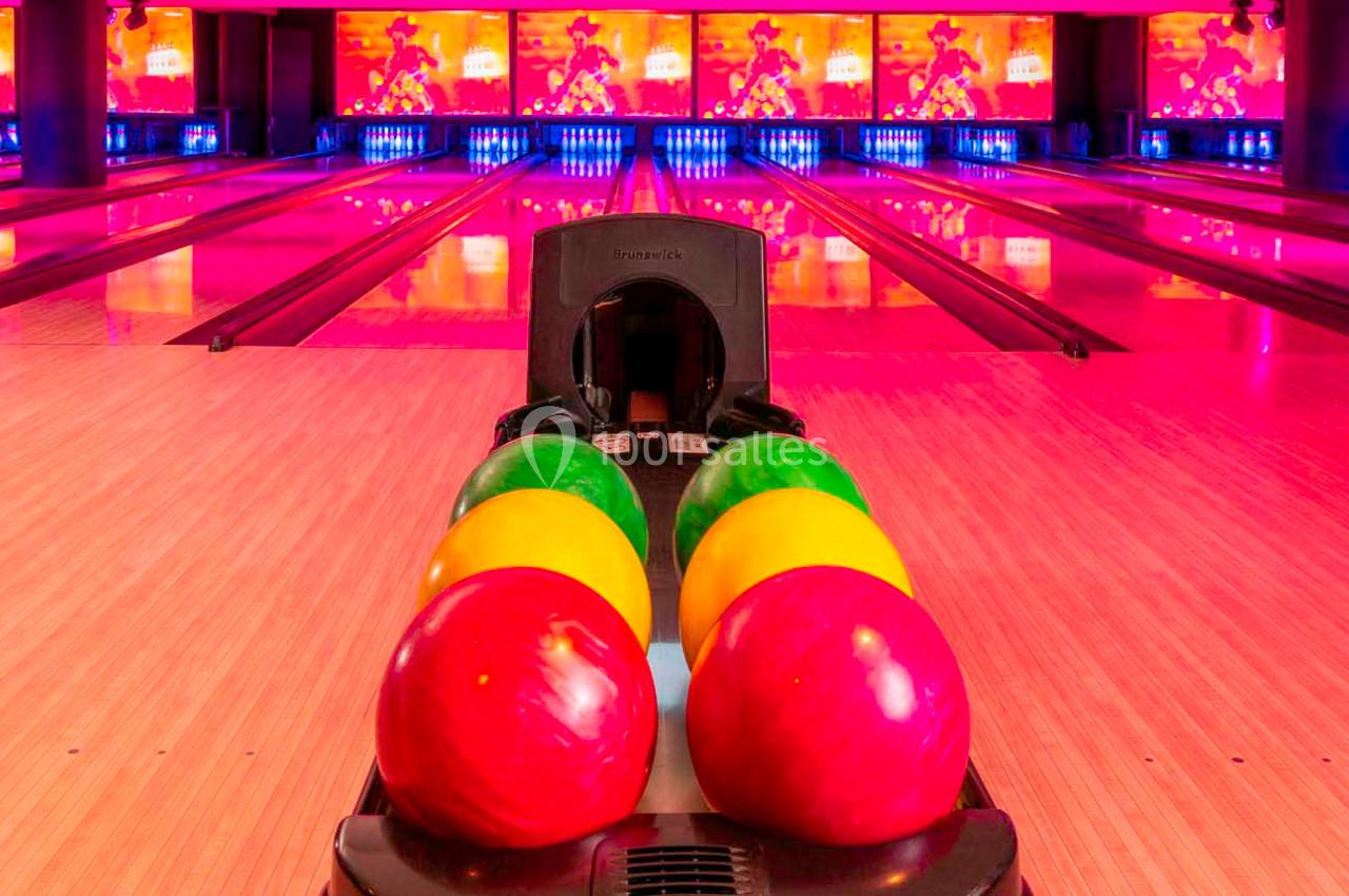 Quatre boules de bowling colorées alignées sur une rampe devant des pistes éclairées par des lumières roses.