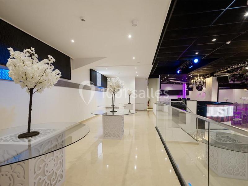 Salle lumineuse avec tables rondes en verre, décorées de petits arbres blancs, et éclairage moderne en arrière-plan.