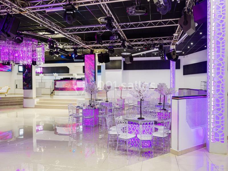 Salle de réception moderne avec tables décorées, chaises transparentes et éclairage violet.