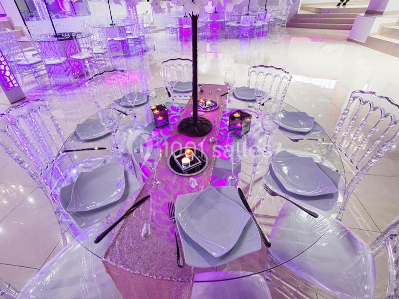 Table ronde élégamment dressée avec assiettes blanches, couverts noirs, bougies et décorations violettes dans une salle…