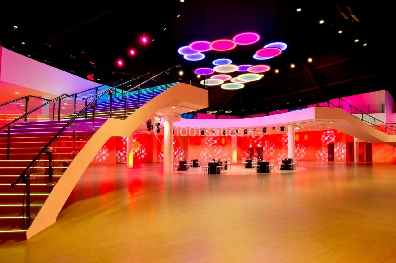 Salle spacieuse avec escalier moderne, éclairage coloré au plafond et ambiance lumineuse rouge et rose.