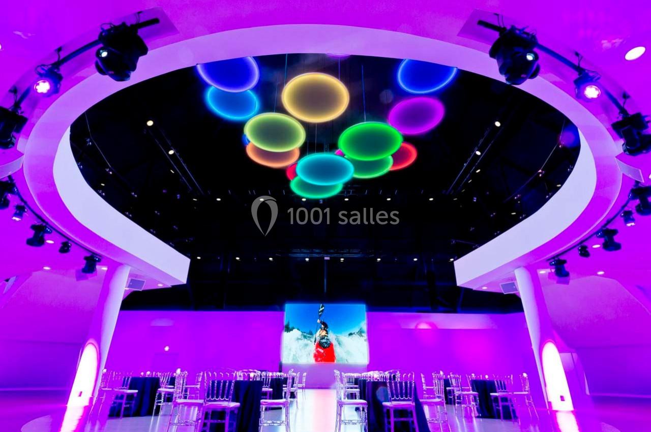 Salle moderne éclairée de lumières violettes, avec des tables et des chaises transparentes, et des cercles lumineux…