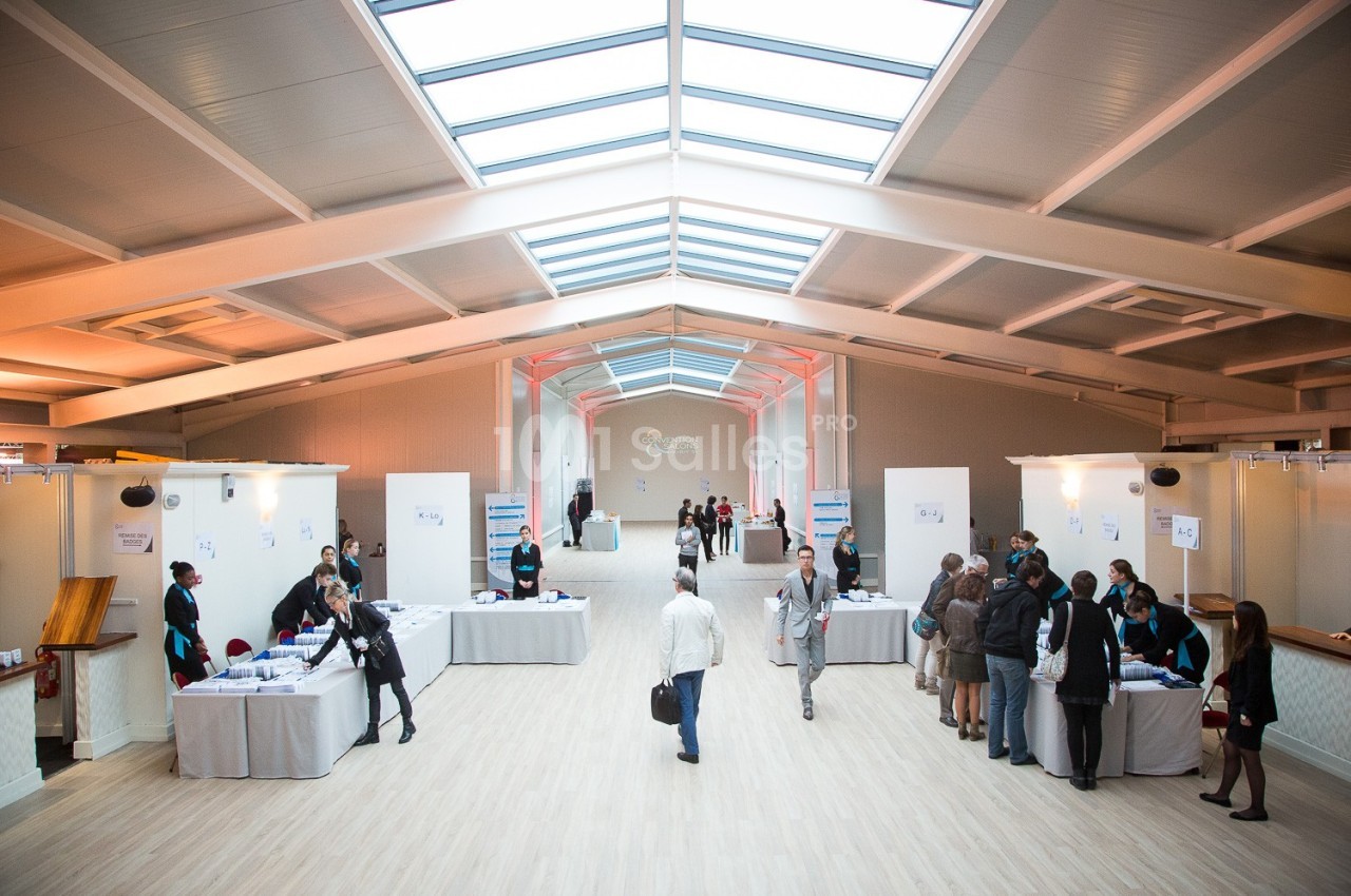 Vue d'une salle d'exposition lumineuse avec des stands alignés et des visiteurs en interaction.
