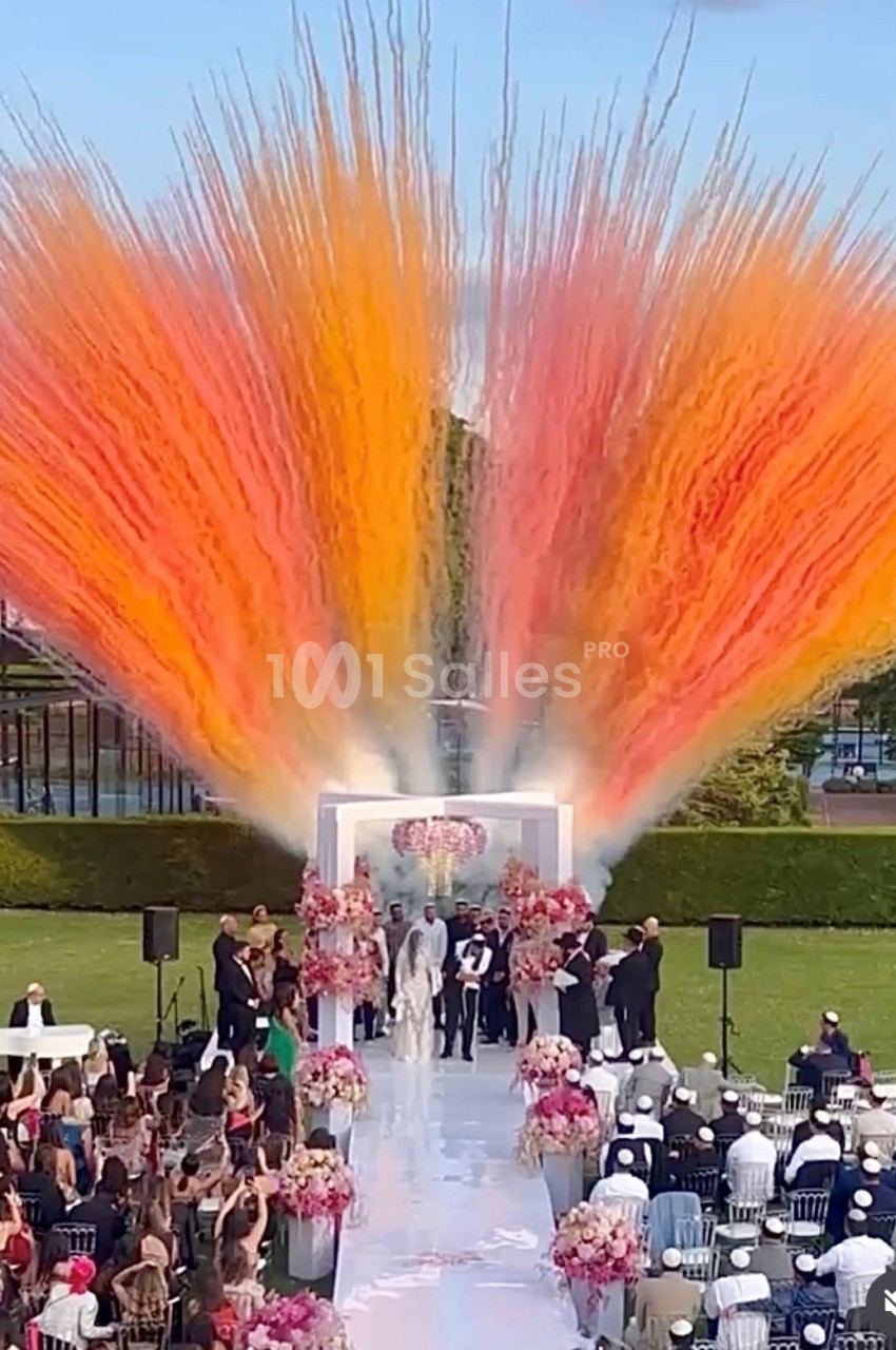 Cérémonie de mariage en plein air avec des jets de fumée colorée orange et rouge en arrière-plan.