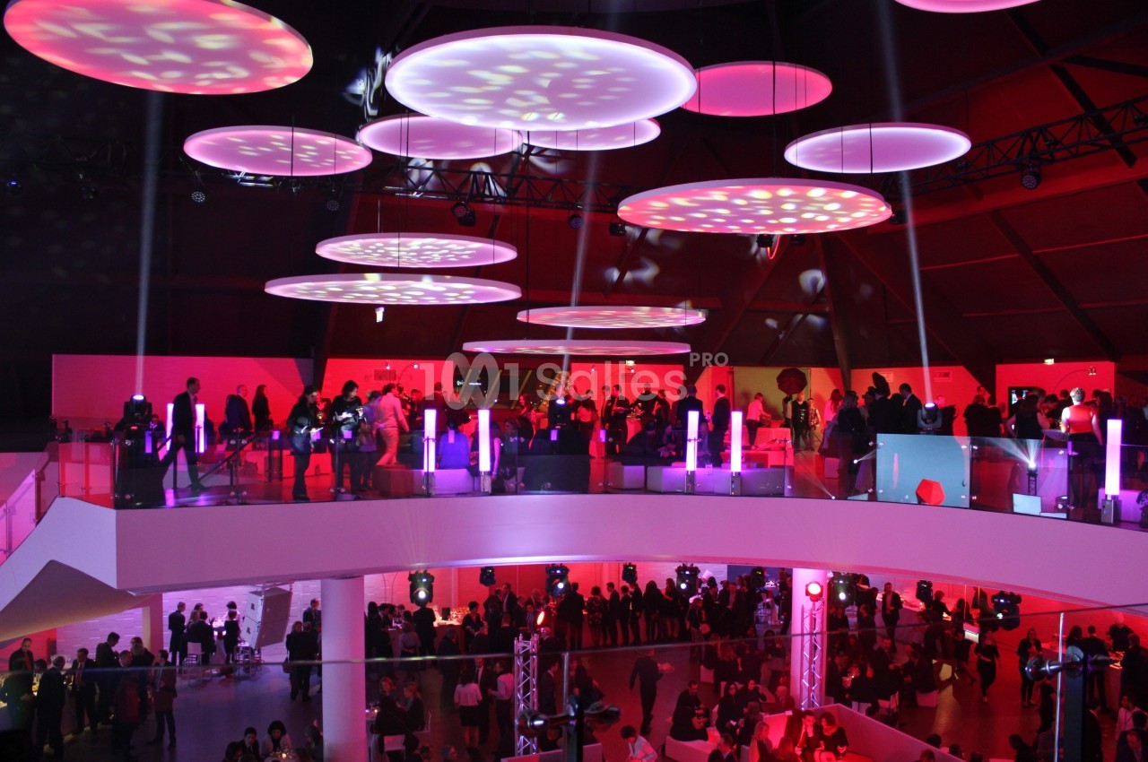 Salle événementielle moderne avec éclairage rouge et violet, remplie de participants sur deux niveaux.