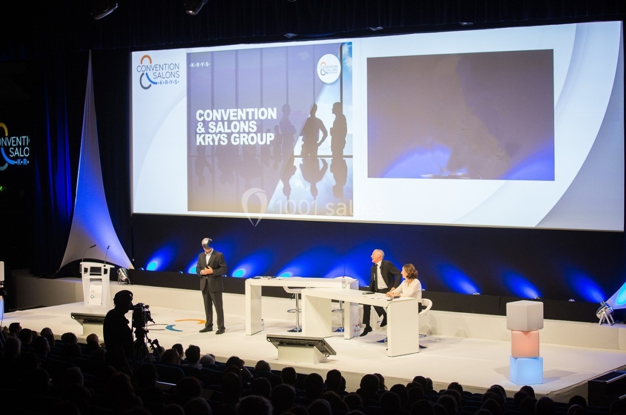 Conférenciers sur scène lors d'un événement professionnel avec une présentation projetée en arrière-plan.