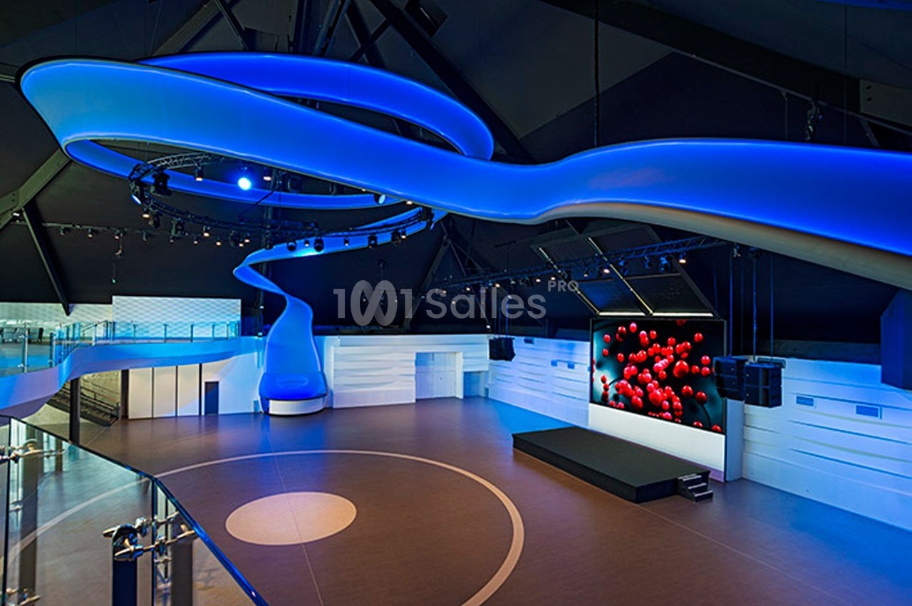 Salle moderne avec éclairage bleu, écran géant affichant des sphères rouges et espace central ouvert.