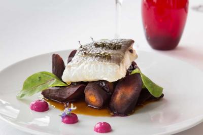 Dessert en forme de cœur au chocolat sur une assiette blanche, accompagné de coulis rouge et d'une verrine en arrière-plan.
