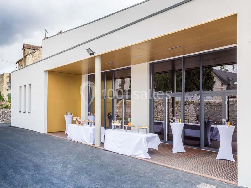 Terrasse d'un bâtiment moderne avec tables dressées pour un événement, nappes blanches et baies vitrées.