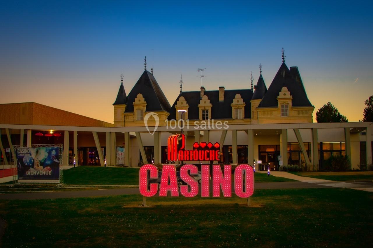 Façade d'un casino avec enseigne lumineuse rouge et bâtiment de style château en arrière-plan, au crépuscule.