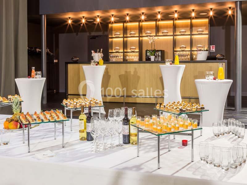 Location salle La Roche-Posay (Vienne) - Casino de la Roche Posay #9 Buffet avec verrines, bouteilles de vin, jus d'orange et tables hautes dans une salle lumineuse avec un bar en arrière-plan.
