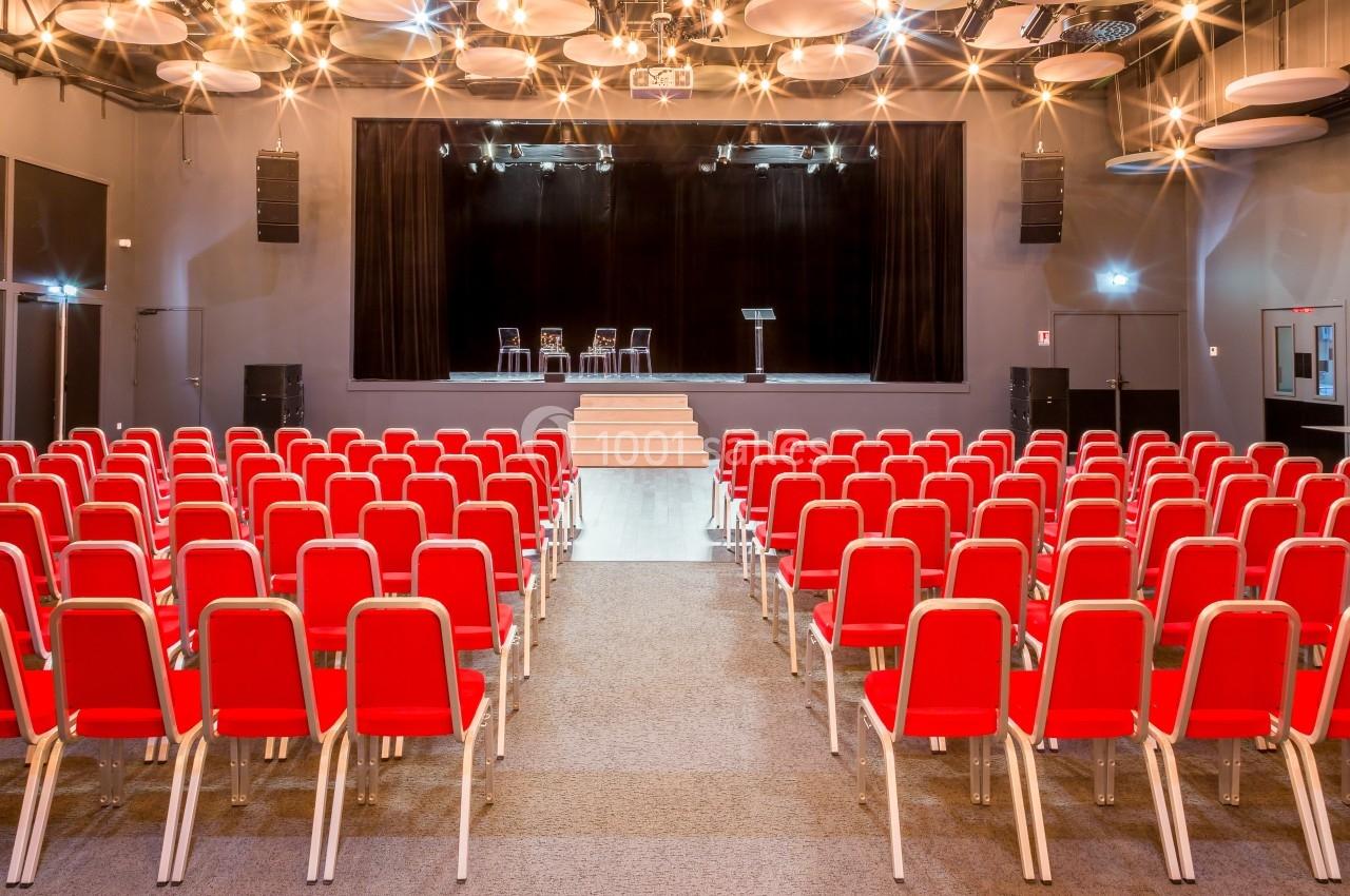Location salle La Roche-Posay (Vienne) - Casino de la Roche Posay #4 Salle de conférence avec des rangées de chaises rouges face à une scène équipée de chaises et d'un pupitre.