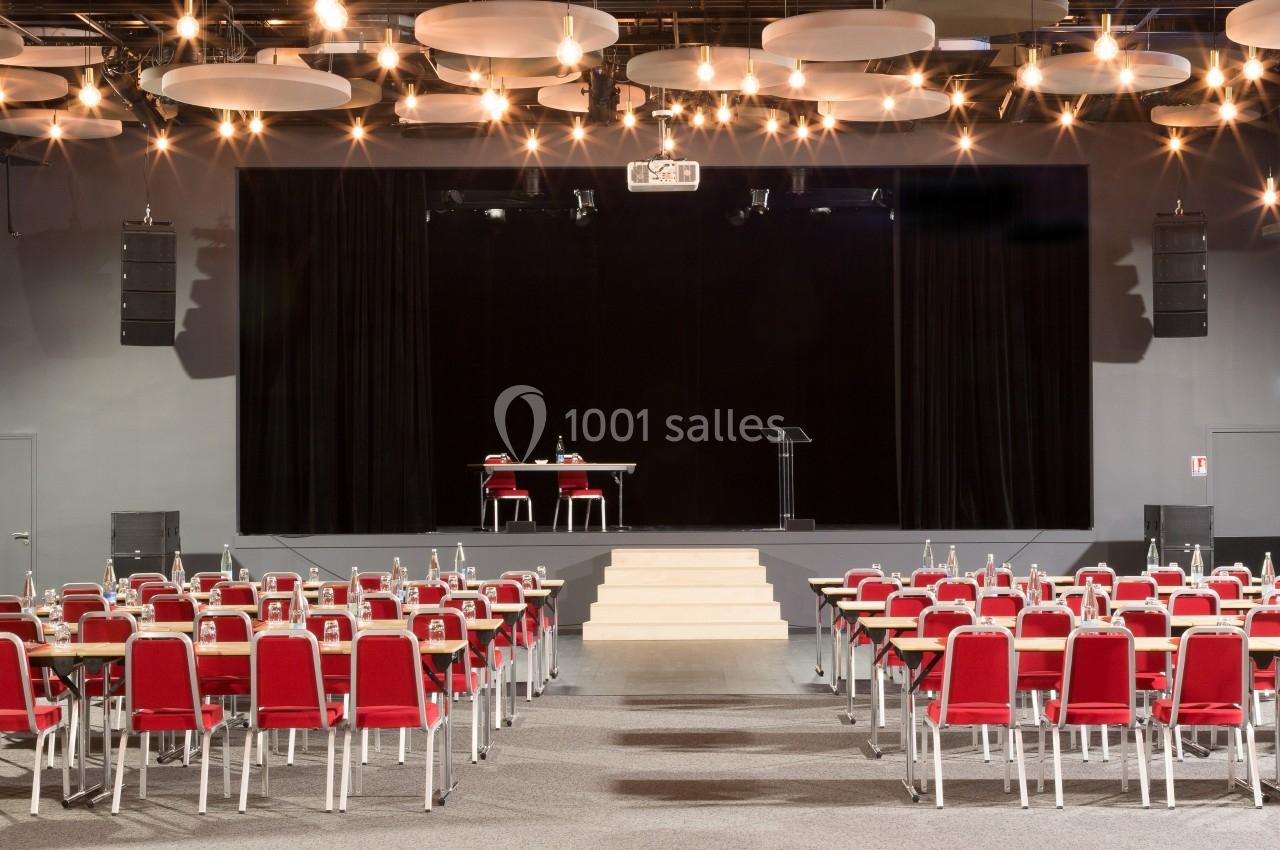 Location salle La Roche-Posay (Vienne) - Casino de la Roche Posay #8 Salle de conférence avec des rangées de chaises rouges, une scène équipée d'une table, de chaises et d'un pupitre.