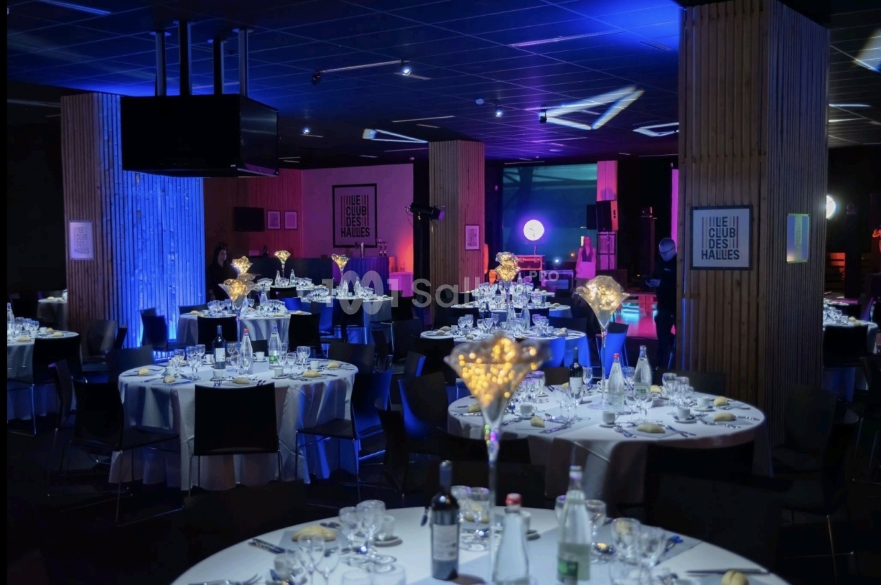 Salle de réception décorée avec des tables rondes dressées, éclairage tamisé et ambiance lumineuse bleutée.