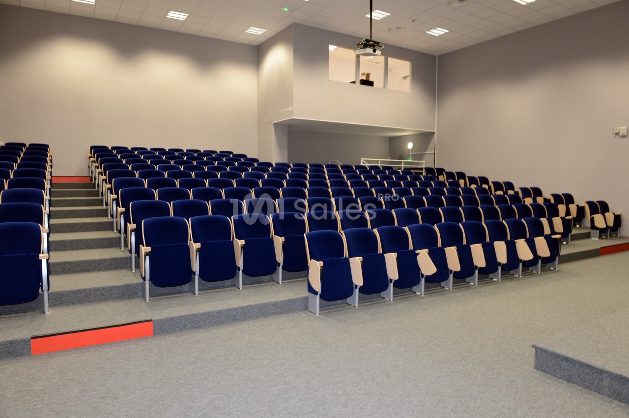Salle de conférence vide avec des rangées de sièges bleus et un projecteur suspendu au plafond.