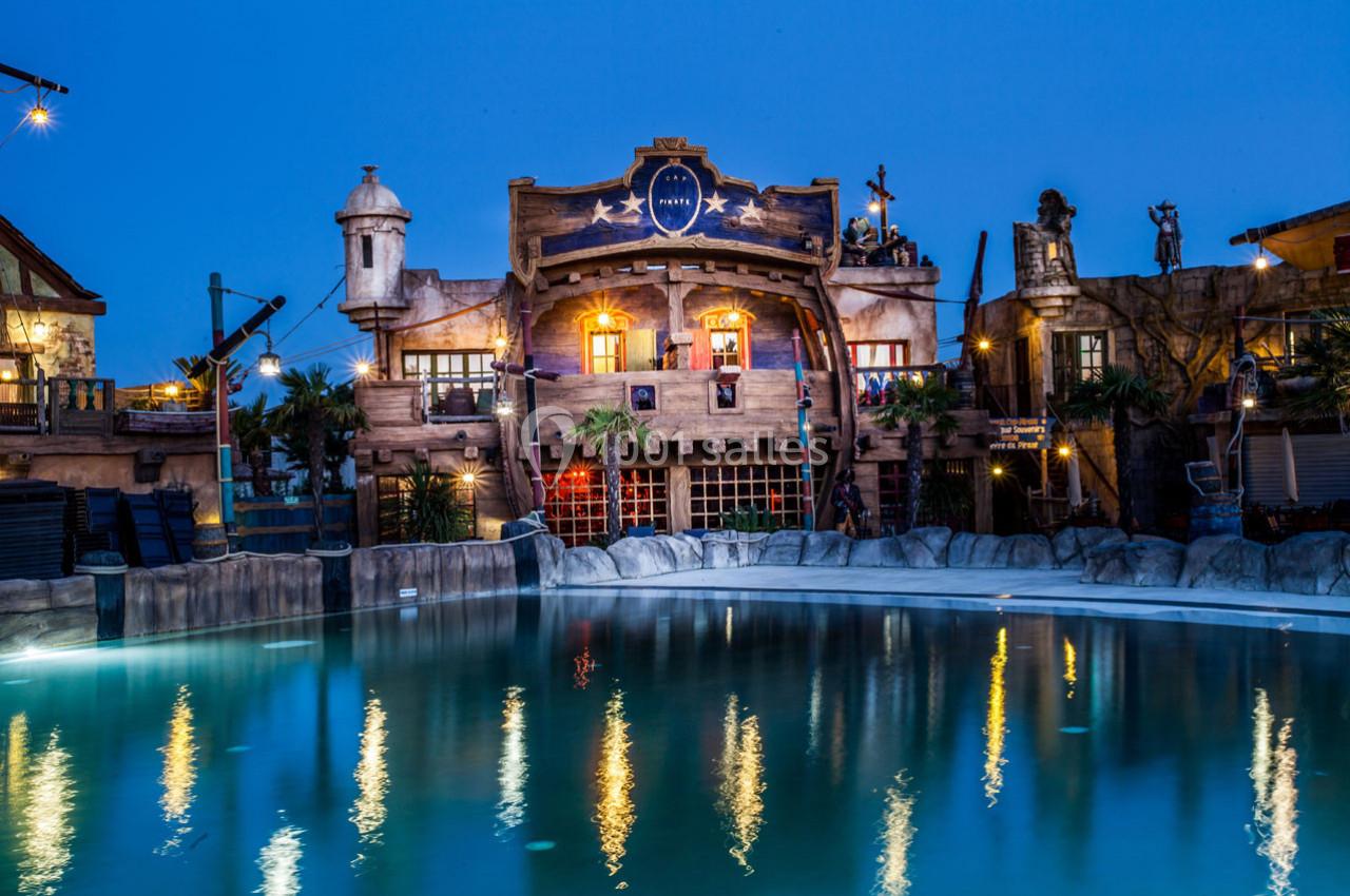 Façade d'un bâtiment à thème pirate éclairé la nuit, avec une piscine calme au premier plan.