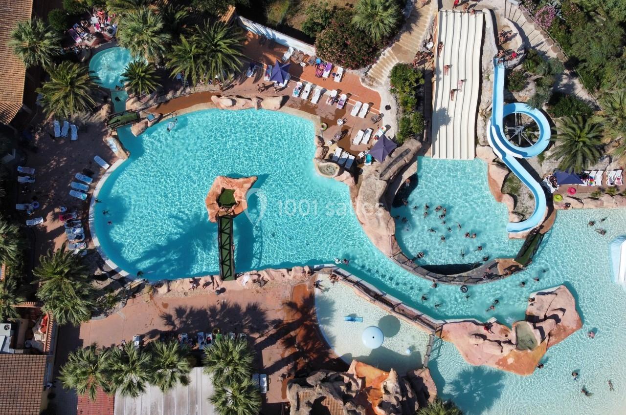 Vue aérienne d'un parc aquatique avec piscines, toboggans, rochers artificiels et espaces de détente entourés de végétation.