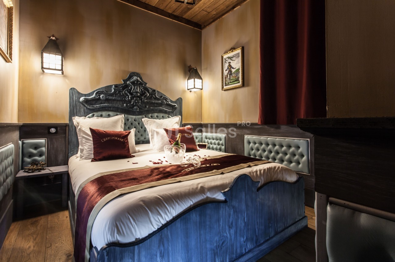 Chambre décorée avec un lit double, draps blancs, coussins rouges, éclairage tamisé et détails en bois et cuir capitonné.