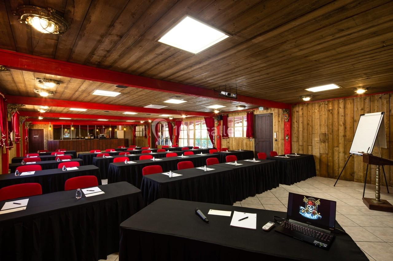 Salle de conférence avec des tables couvertes de nappes noires, chaises rouges, un projecteur et un tableau de présentation.