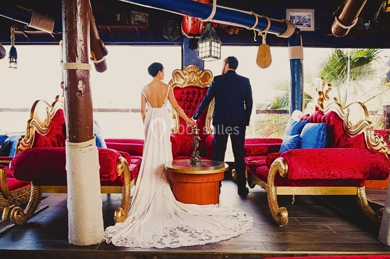 Un couple en tenue de mariage se tient debout dans un salon décoré de fauteuils rouges et dorés.