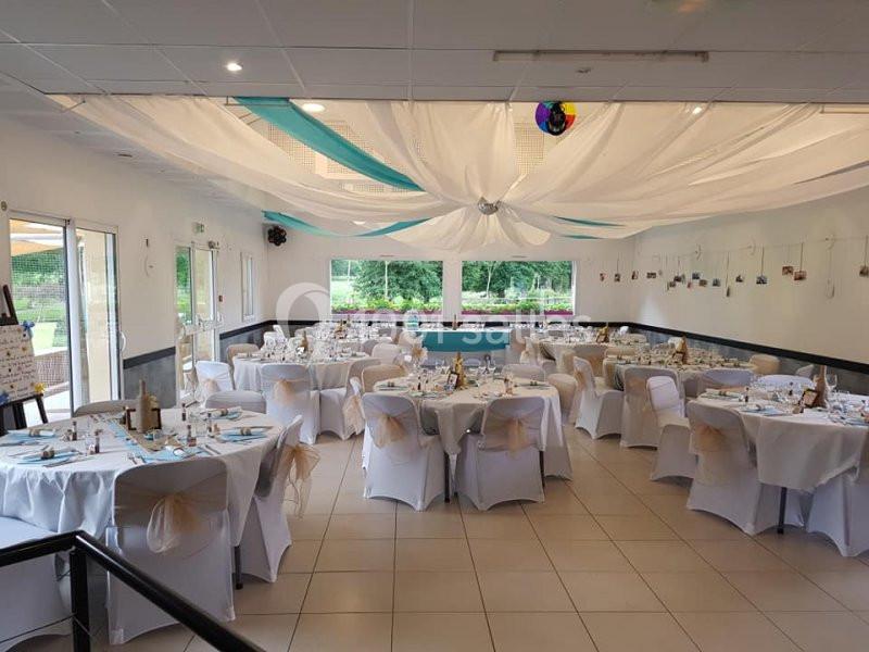 Salle de réception décorée avec des tables rondes dressées, nappes blanches et voilages suspendus au plafond.