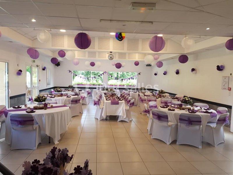 Salle de réception décorée dans des tons violets avec des tables dressées et des lanternes suspendues au plafond.