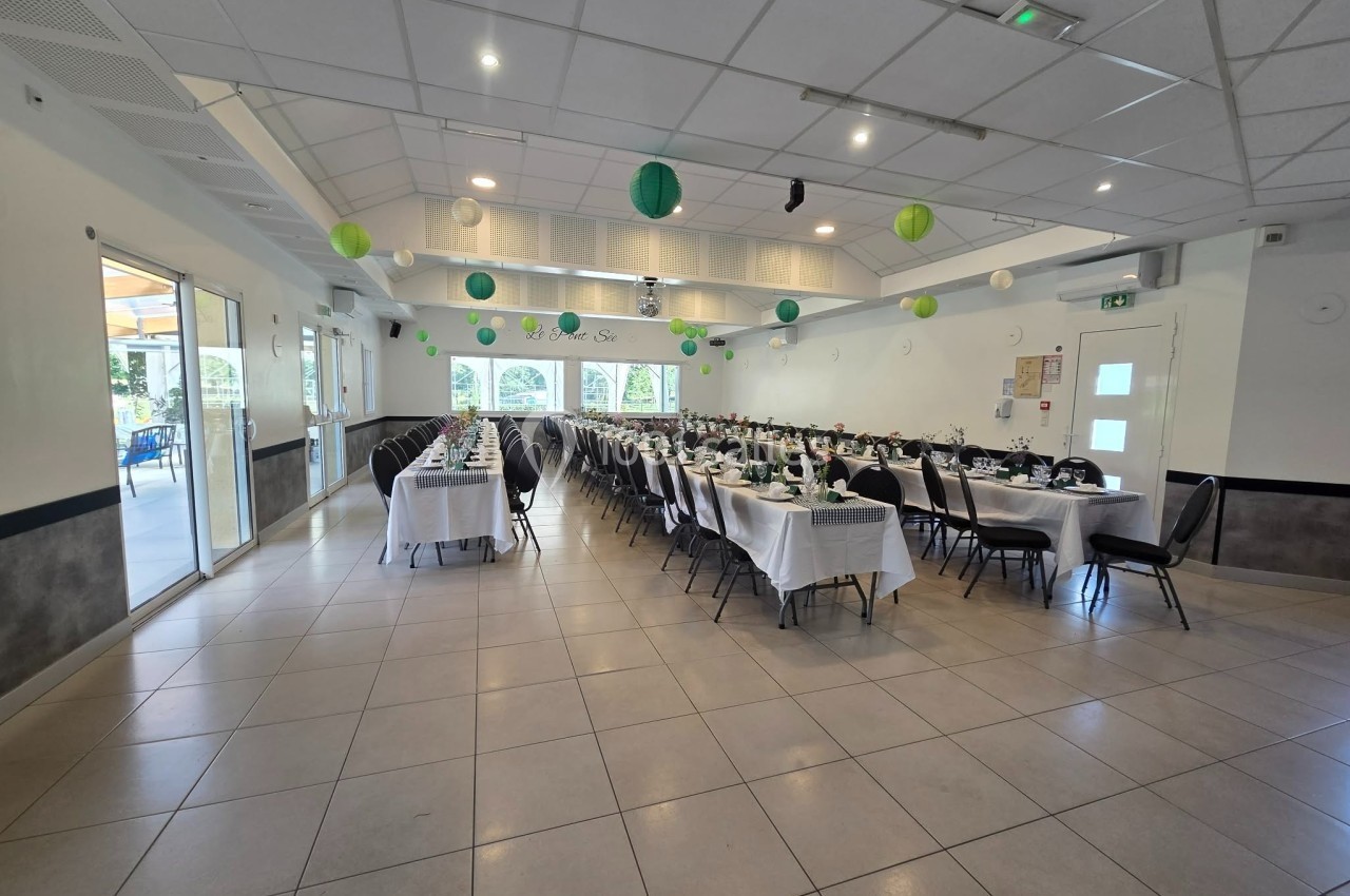 Salle de réception décorée avec des tables alignées, nappes blanches et lanternes suspendues vertes et blanches.