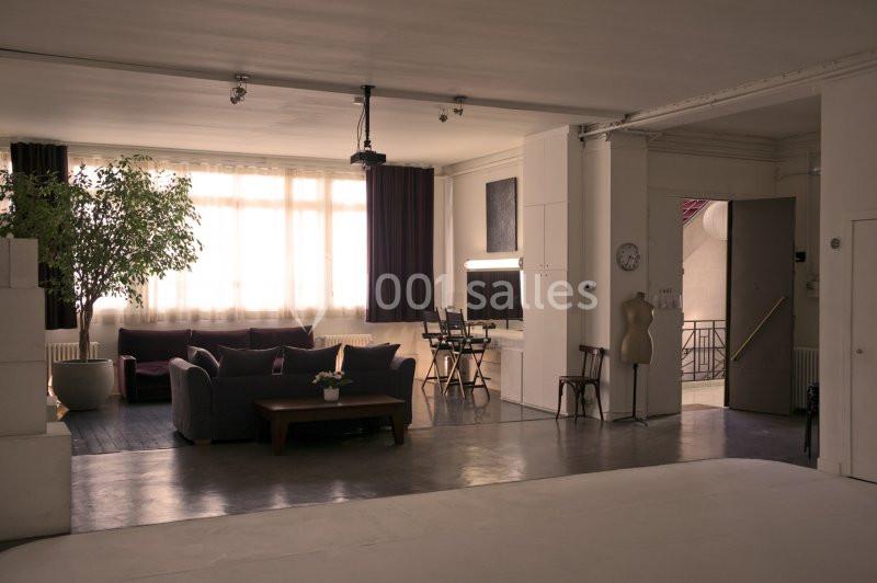 Espace intérieur lumineux avec canapé, table basse, plantes, bureau et mannequin de couture près d'une porte ouverte.