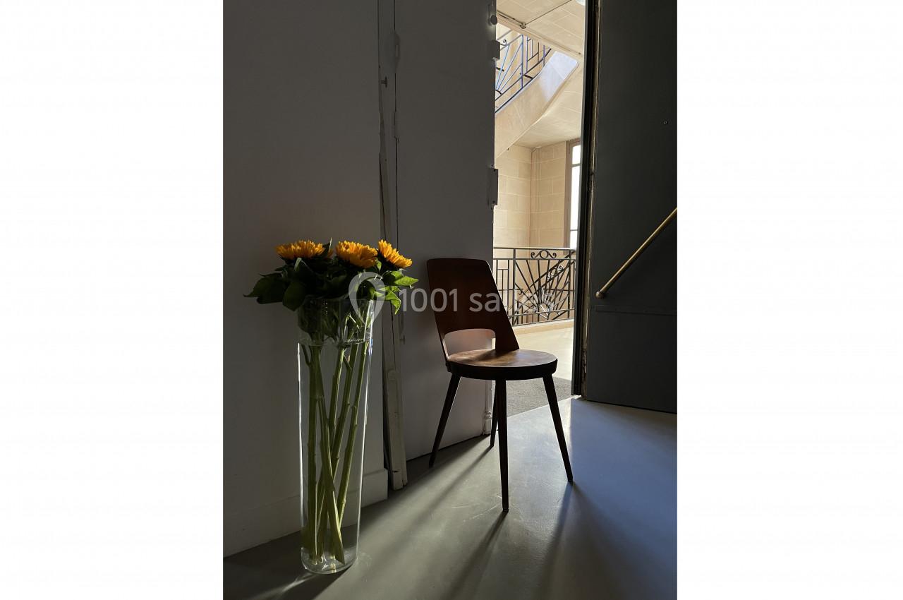 Vase de tournesols posé à côté d'une chaise en bois, éclairés par une lumière naturelle dans un intérieur minimaliste.