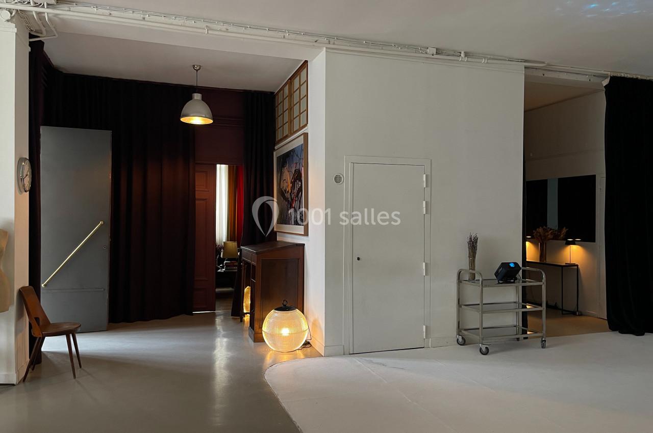 Espace intérieur avec murs blancs, rideaux sombres, mobilier minimaliste et éclairage tamisé.
