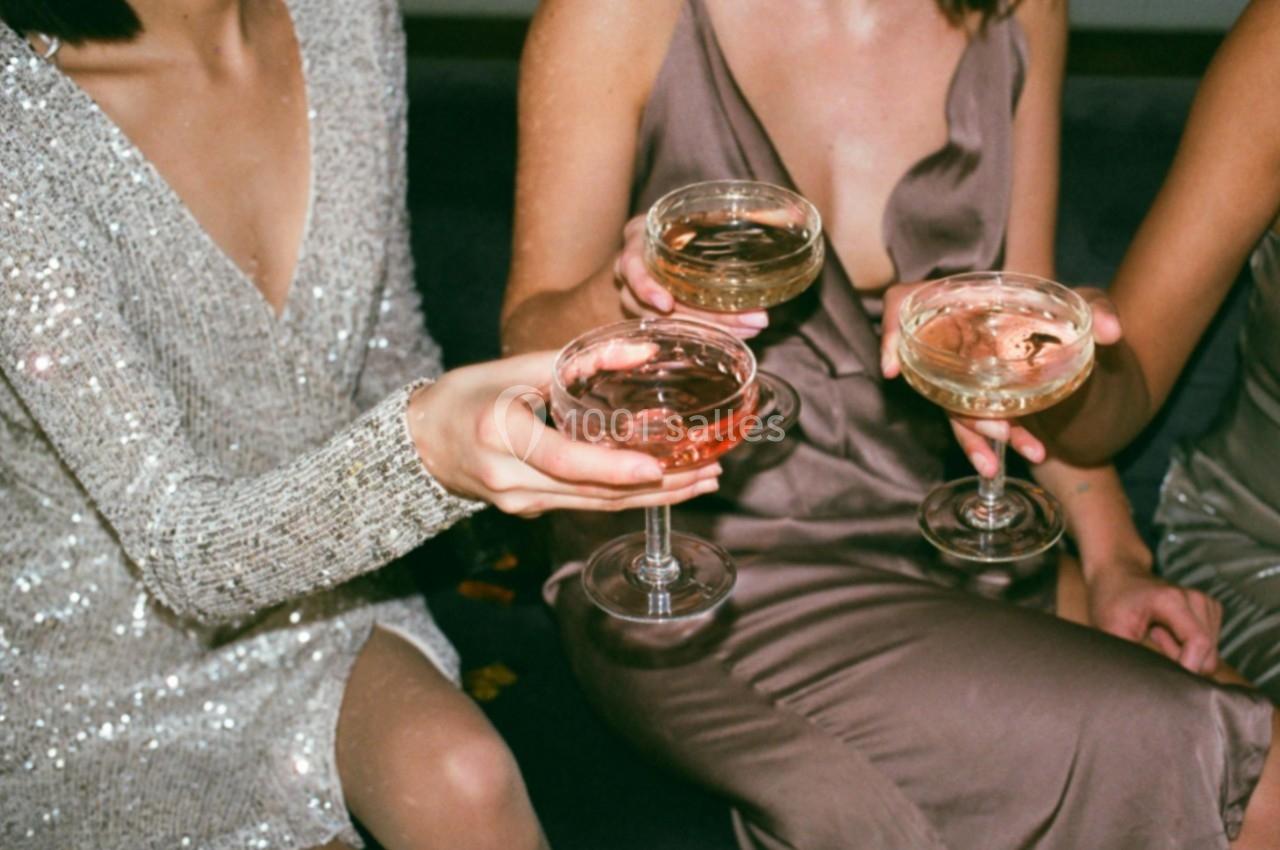 Trois personnes en tenue élégante trinquent avec des coupes de champagne remplies de boissons colorées.