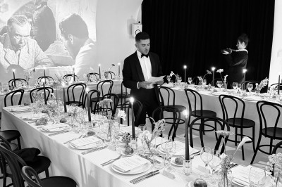 Grand arbre en pot éclairé par une lumière verte dans un salon moderne avec canapé, tables et vases de fleurs.