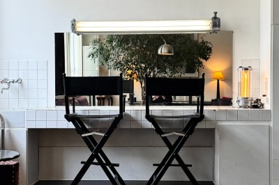 Grand arbre en pot éclairé par une lumière verte dans un salon moderne avec canapé, tables et vases de fleurs.