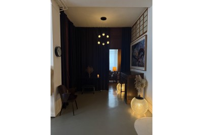 Grand arbre en pot éclairé par une lumière verte dans un salon moderne avec canapé, tables et vases de fleurs.