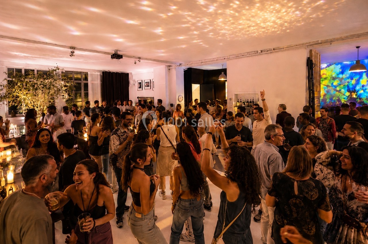 Location salle Paris 20 (Paris) - Studio 7 #11 Groupe de personnes dans une salle animée, dansant et discutant sous des lumières tamisées et festives.