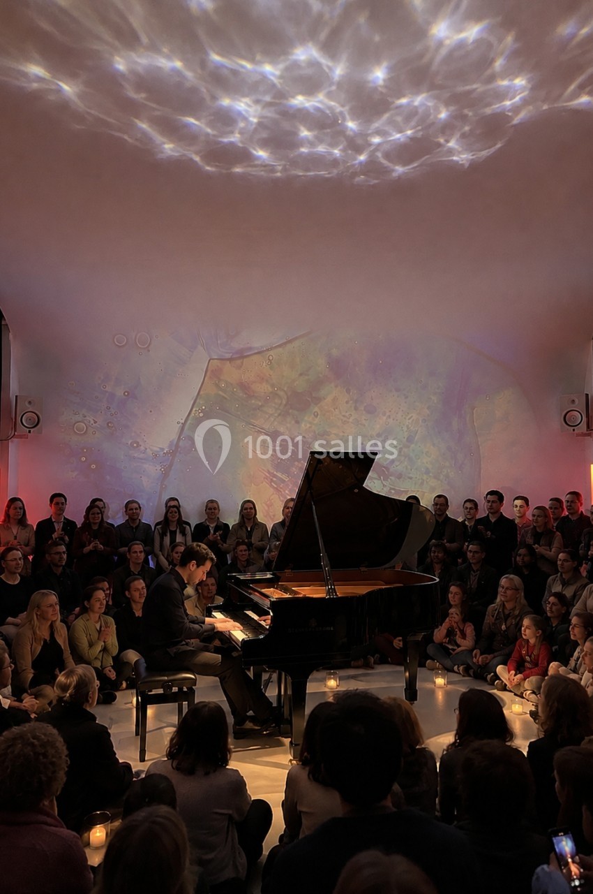 Location salle Paris 20 (Paris) - Studio 7 #25 Un pianiste joue sur un piano à queue devant un public assis dans une salle à l'éclairage tamisé.