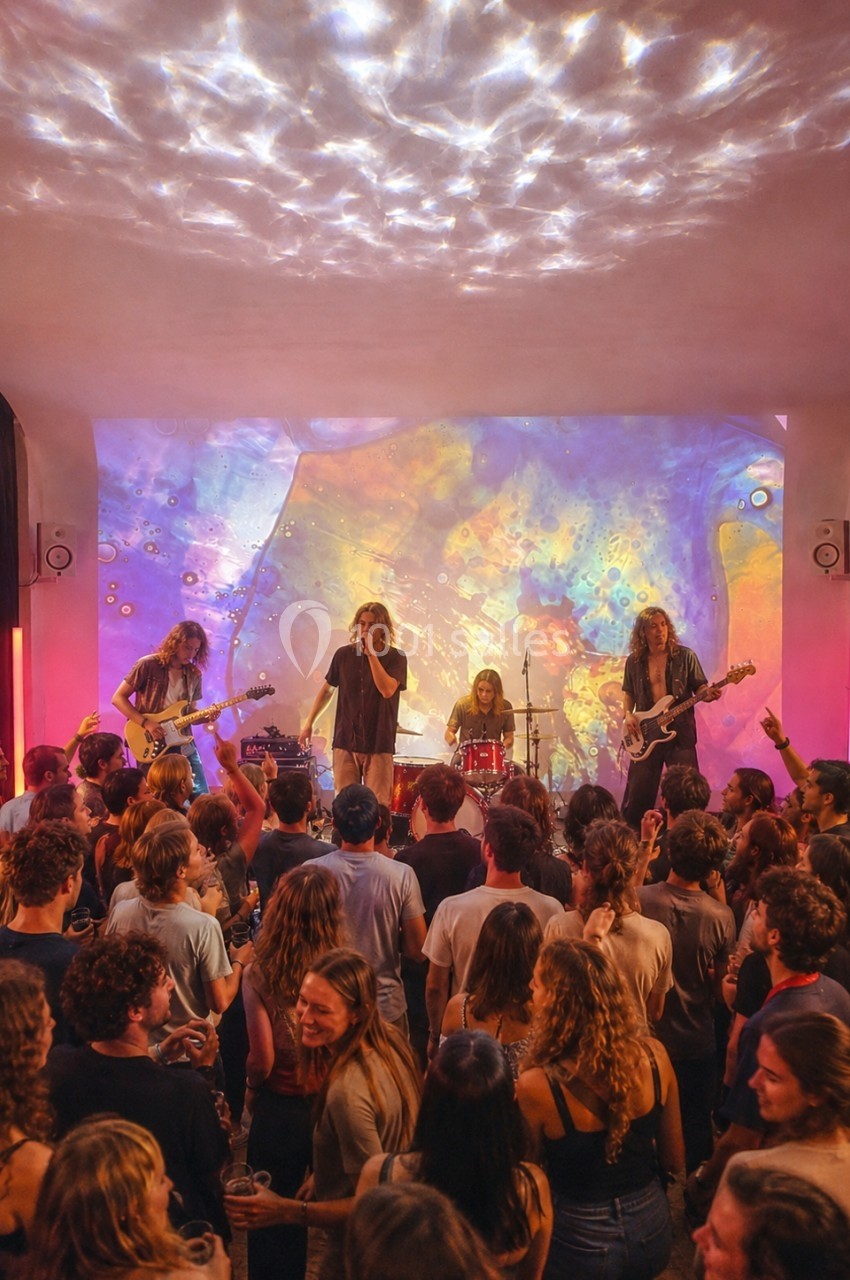 Location salle Paris 20 (Paris) - Studio 7 #16 Groupe de musiciens jouant sur scène devant une foule, éclairés par des projections lumineuses colorées.