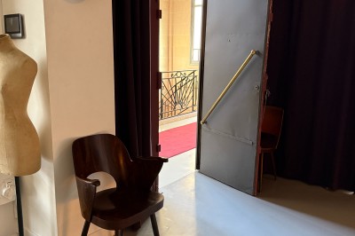 Miniature Location salle Paris 20 (Paris) - Studio 7 #49 Une chaise en bois et un mannequin près d'une porte ouverte donnant sur un couloir lumineux avec une rambarde en fer forgé.